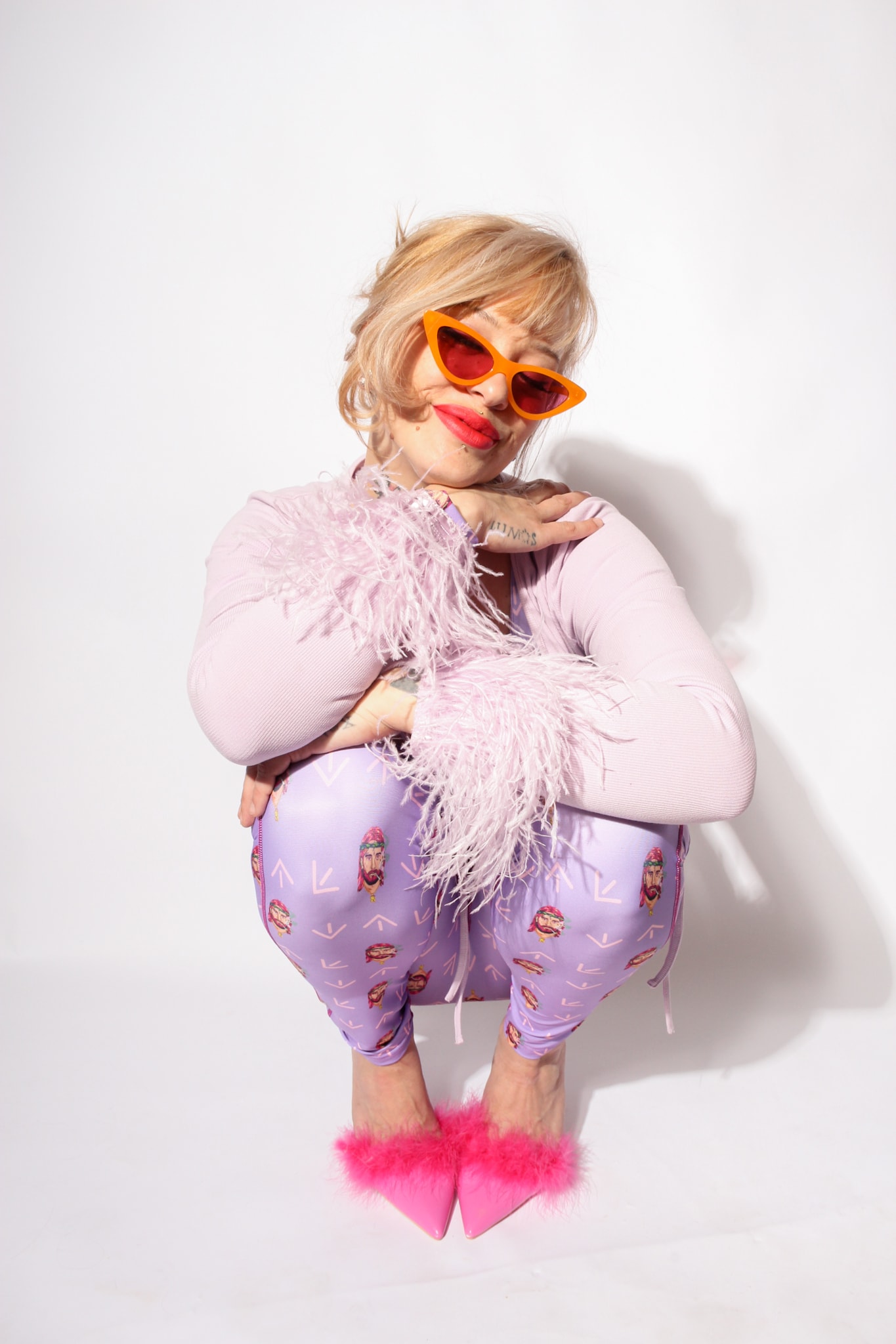 South North Southwest crouching with arms crossed in a lilac catsuit