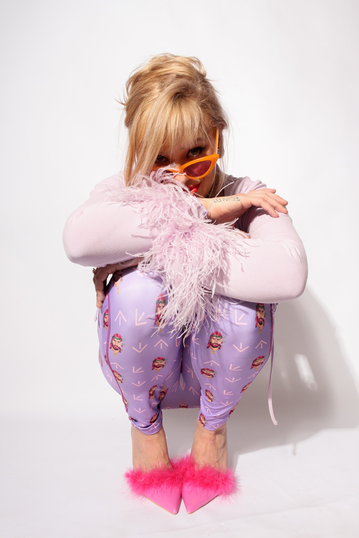 South North Southwest crouching in a lilac catsuit with a feather boa